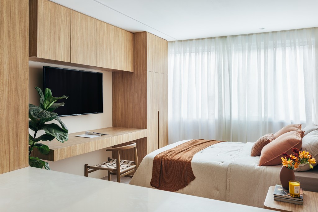 Projeto de Rodolfo Consoli. Na foto, quarto com cabeceira de drywall e azulejos, móvel com painel de tv, armário e bancada de trabalho, cortina branca.