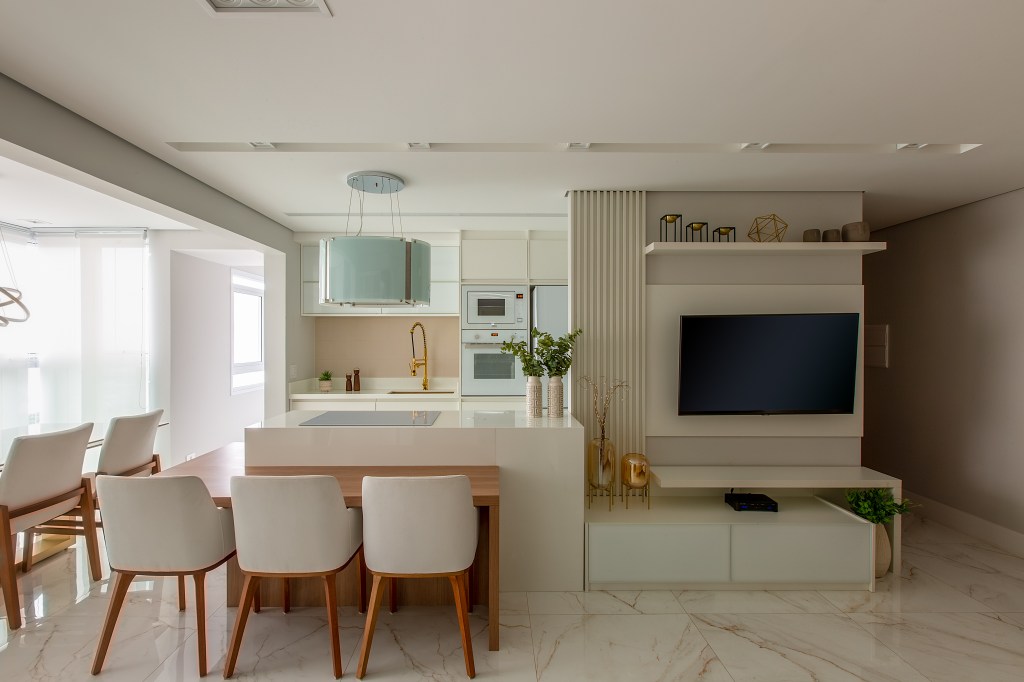 Projeto de Luciana Patriarcha. Na foto, cozinha com marcenaria branca com bancada. Sala de tv integrada.
