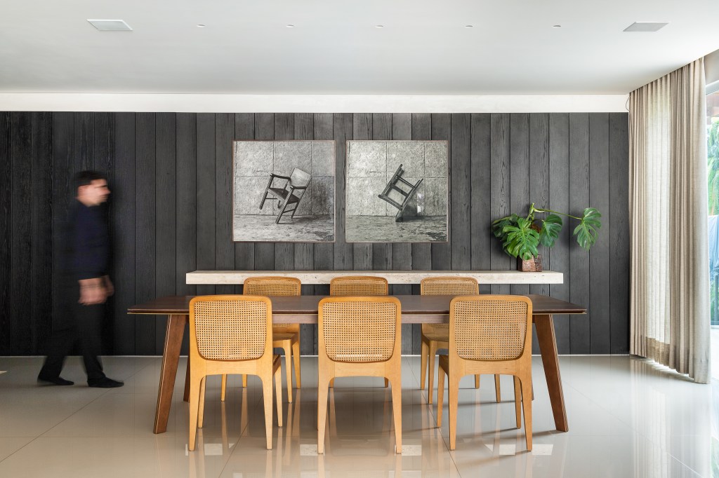Painéis de carvalho ebanizados revestem as paredes deste apê de 320 m². Projeto de Lucas Lage. Na foto, sala de jantar com parede de madeira e quadro.