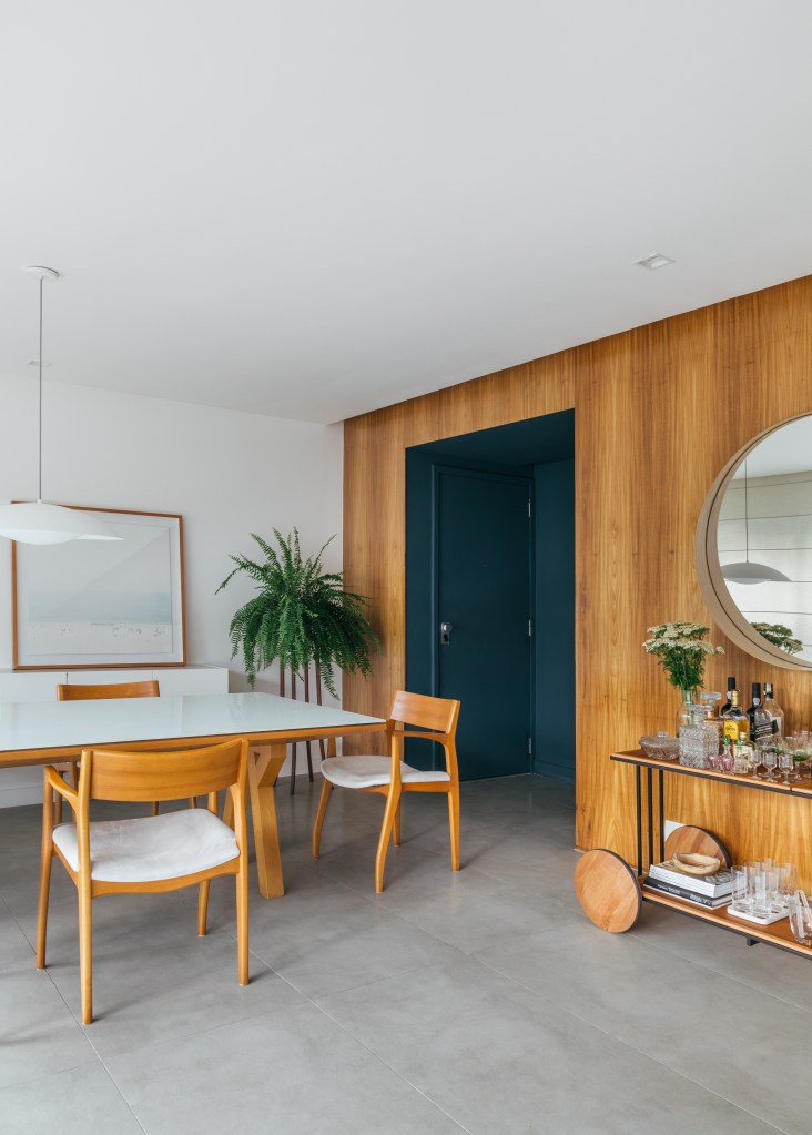 Projeto de A+G Arquitetura. Na foto, sala de jantar com painel de madeira na parede, hall de entrada azul, carrinho de chá.