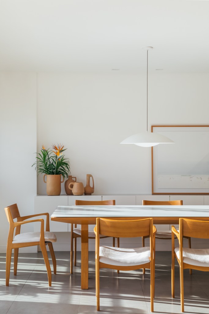 Projeto de A+G Arquitetura. Na foto, sala de jantar com mesa de tampo branco, cadeiras de madeira e buffet branco.