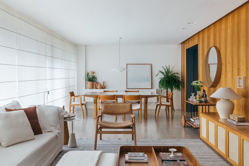 Projeto de A+G Arquitetura. Na foto, sala de estar integrada com jantar com piso de porcelanato e painel de madeira na parede.