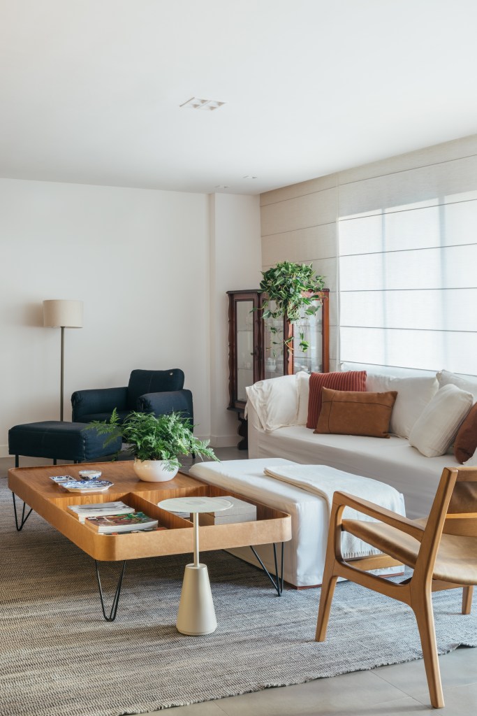 Projeto de A+G Arquitetura. Na foto, sala de estar com sofá branco, pufe branco, persiana, poltrona azul e mesa de centro de madeira.
