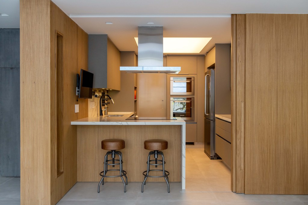 Painéis escondem e revelam ambientes neste apartamento de 130 m². Projeto de Mauricio Nóbrega. Na foto, cozinha com porta de correr e bancada ripada.