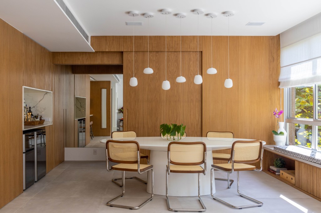 Painéis escondem e revelam ambientes neste apartamento de 130 m². Projeto de Mauricio Nóbrega. Na foto, sala de jantar com portas de correr e banco.