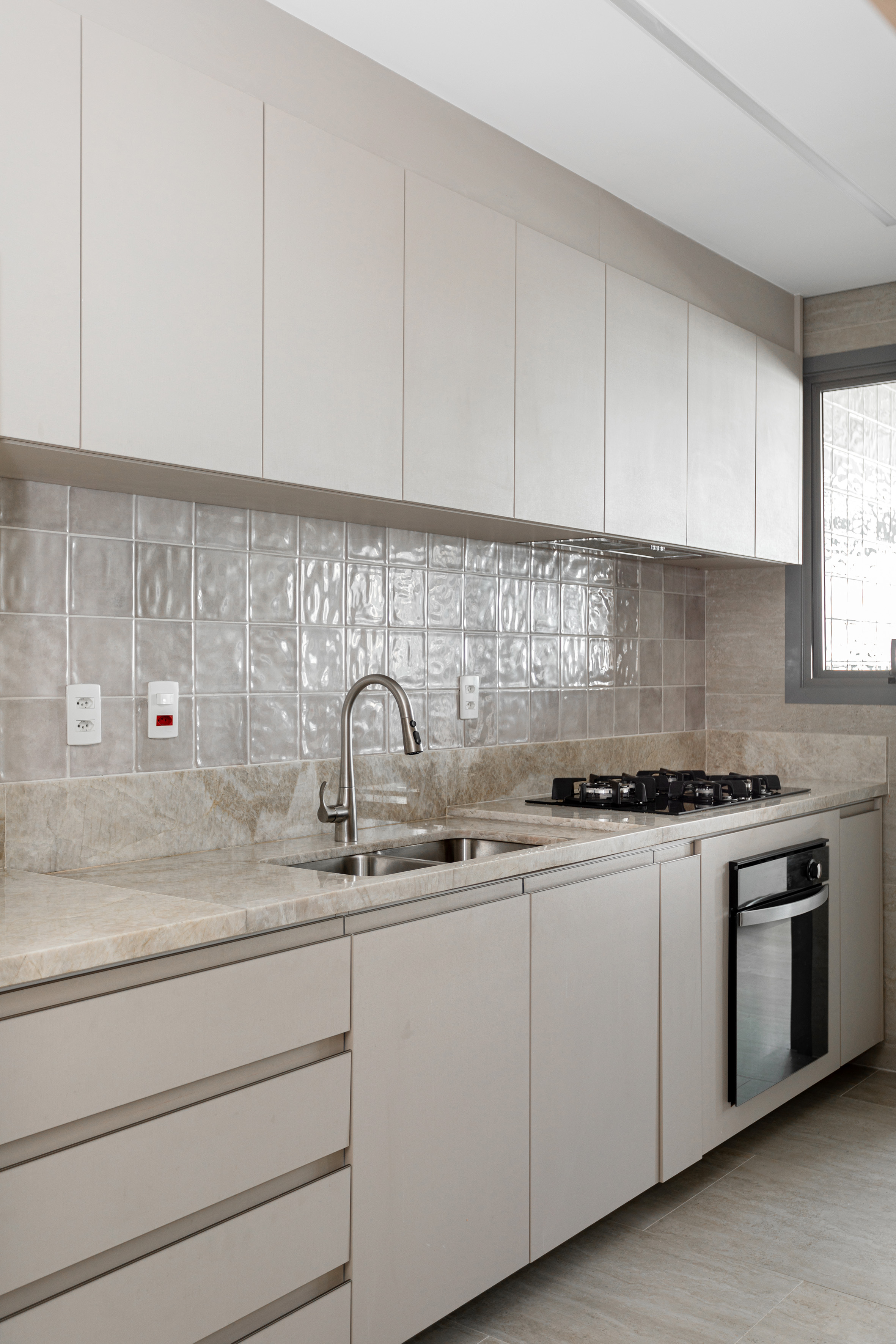 Projeto de NOP Arquitetura. Na foto, cozinha com armários cinza claro e backsplash de azulejos cinzas acinzentados.