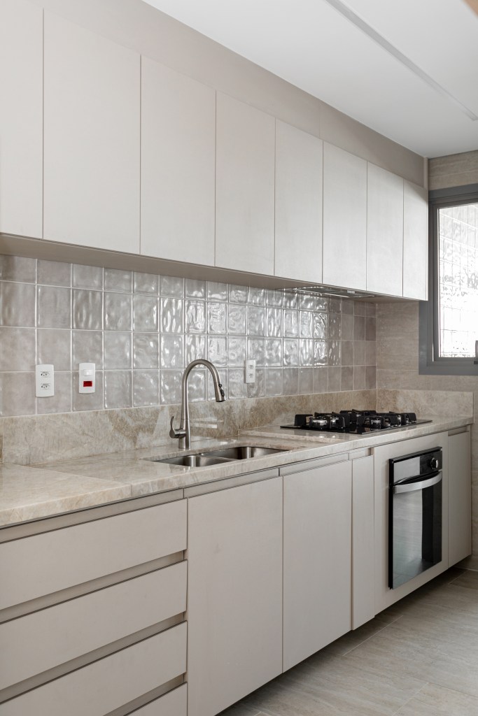 Projeto de NOP Arquitetura. Na foto, cozinha com armários cinza claro e backsplash de azulejos cinzas acinzentados.