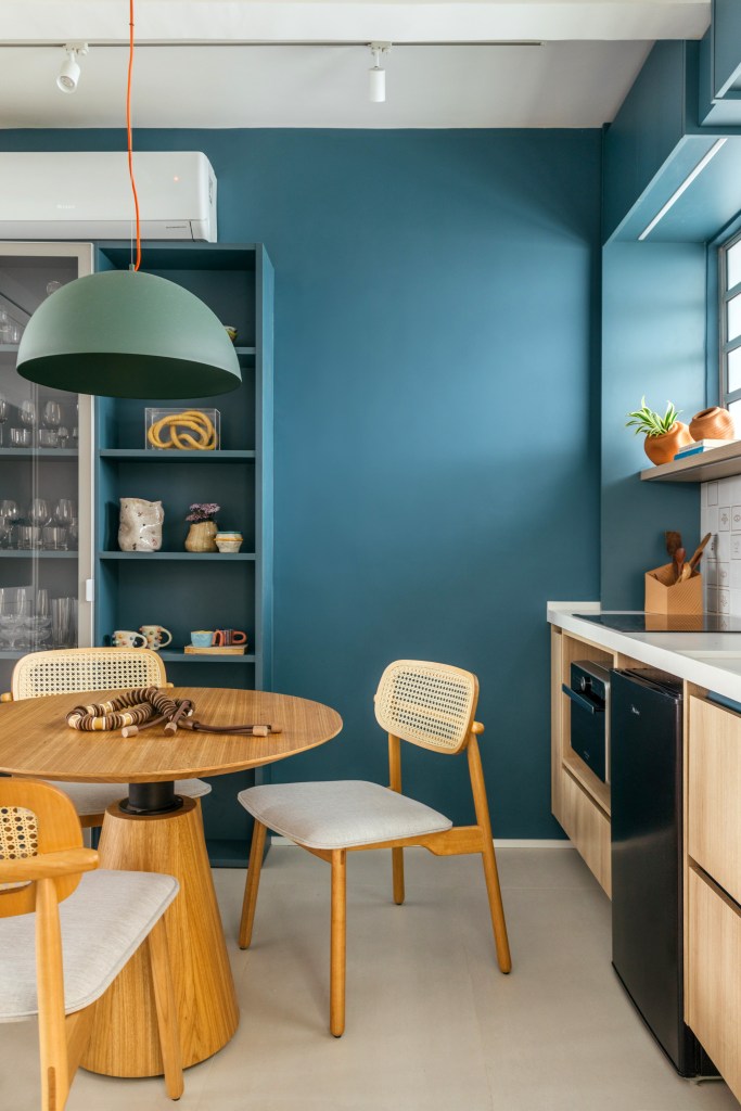 Projeto de Casa Cururu. Na foto, cozinha pequena com parede e marcenaria azul, bancada branca, prateleira e armário emoldurando janela.