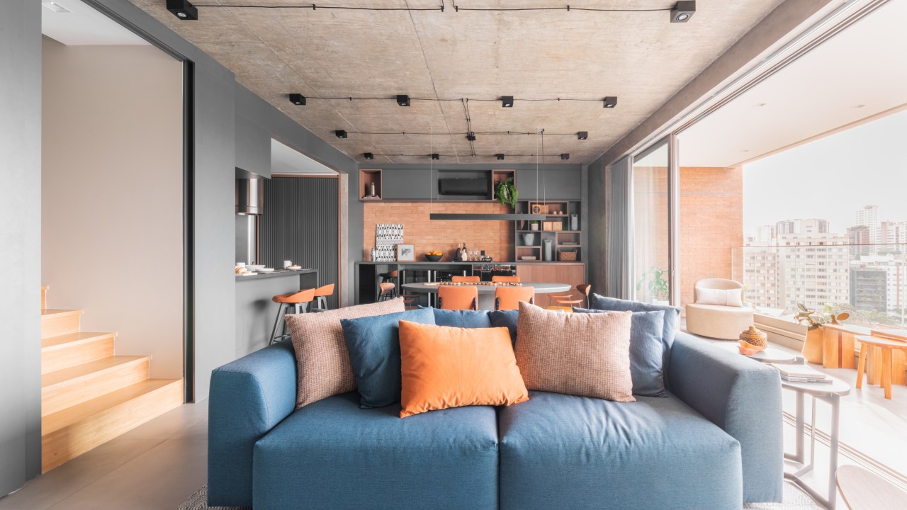 Projeto de BMA Studio. Na foto, sala de estar integrada com cozinha em estilo industrial com sofá azul.