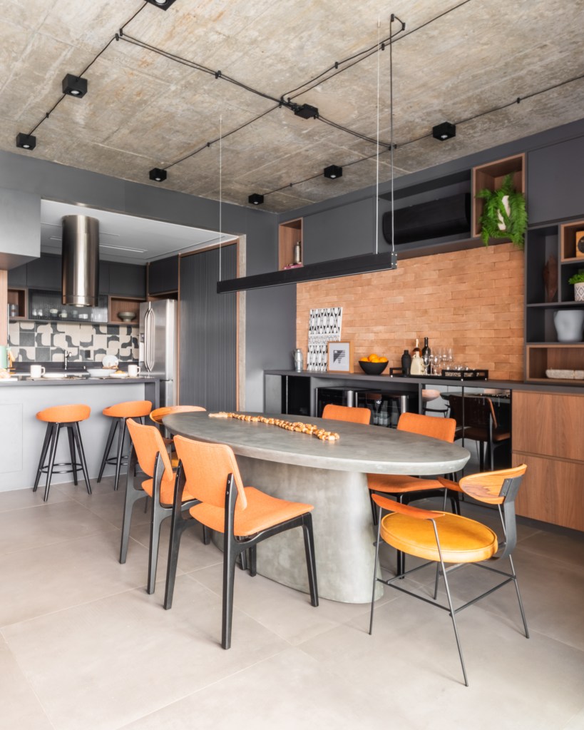 Projeto de BMA Studio. Na foto, sala de jantar integrada com cozinha com mesa oval cinza e cadeiras laranja.