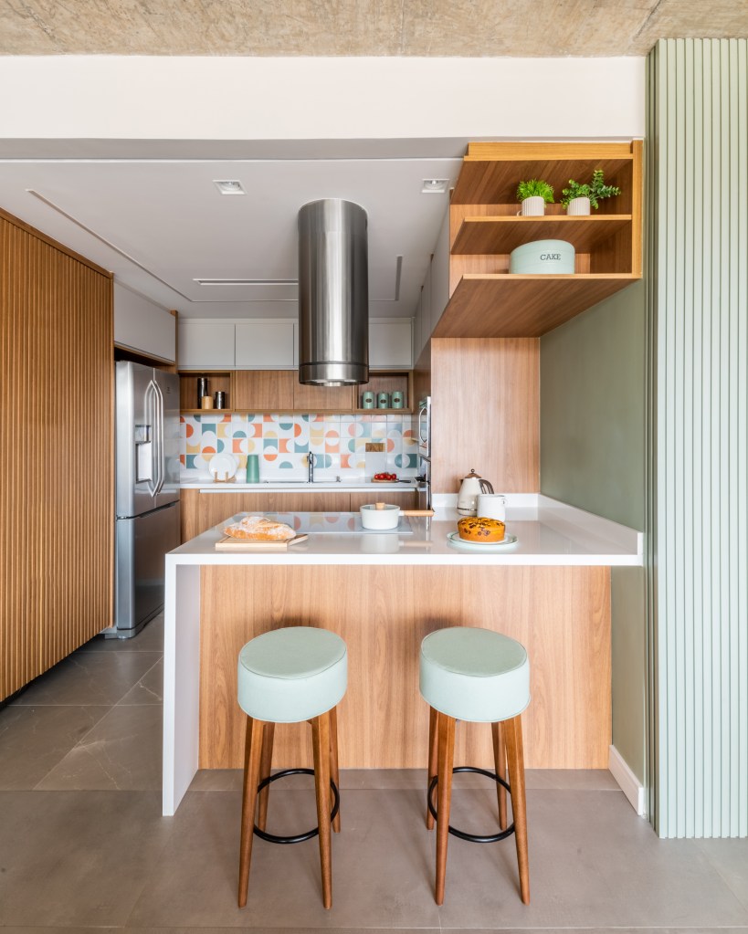 Projeto de BMA Studio. Na foto, cozinha integrada pequena com bancada branca, marcenaria e banqueta verdes claras.