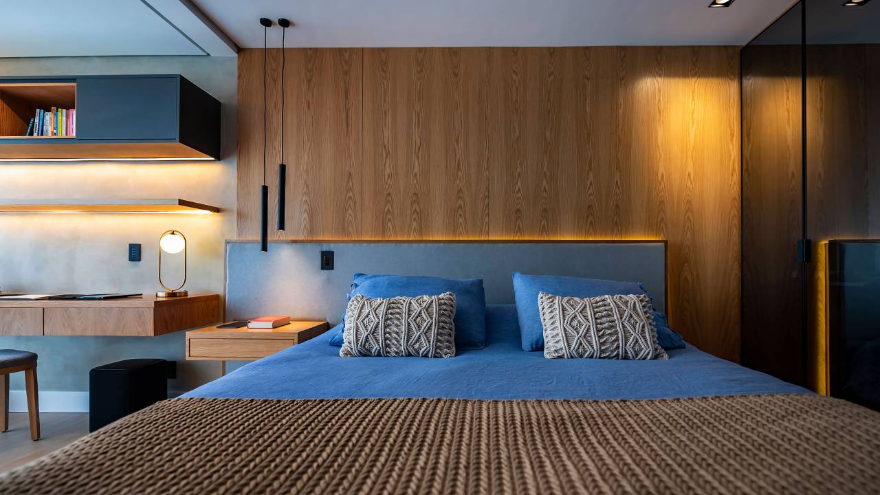 Qual é a iluminação perfeita para deixar o quarto relaxante. Na foto, quarto com cabeceira azul e iluminação embutida na cabeceira.