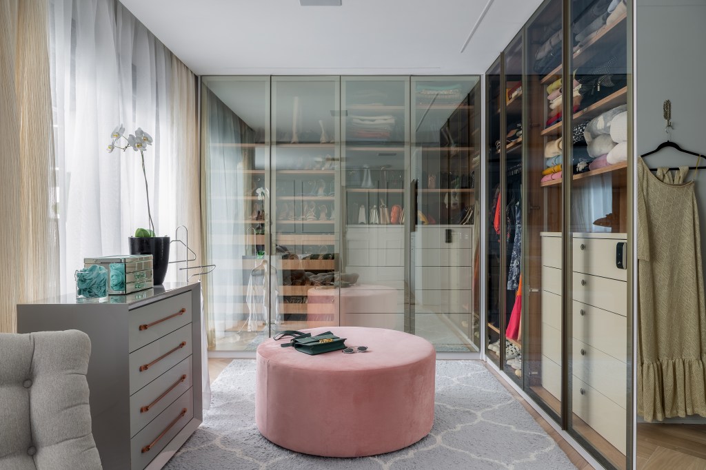 6 Tendências para o closet dos sonhos. Projeto de Spaço Interior. Na foto, closet com portas transparentes e pufe rosa.