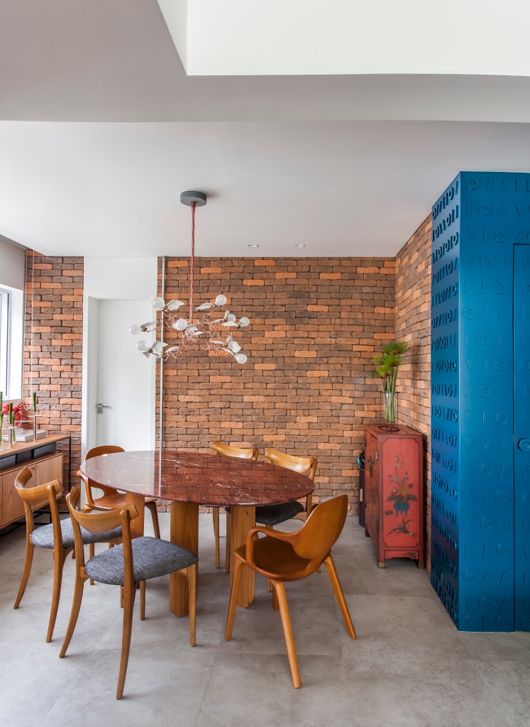 Projeto de Korman Arquitetos. Na foto, sala de jantar com mesa oval, cadeira de madeira e parede de tijolinhos.