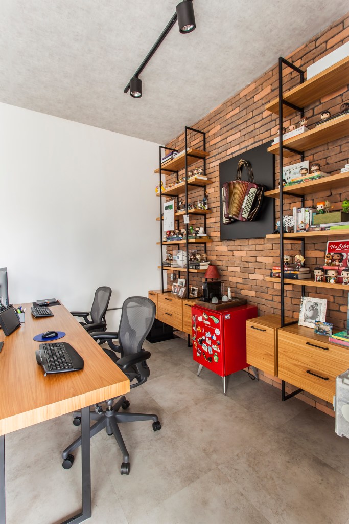 Projeto de Korman Arquitetos. Na foto, home office duplo com parede de tijolinhos e estantes.