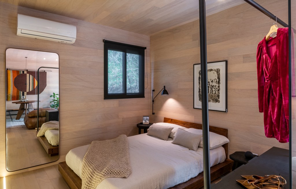 Tiny house sustentável de madeira fica pronta em 1 mês. Na foto, quarto com parede de madeira, armario e espelho.