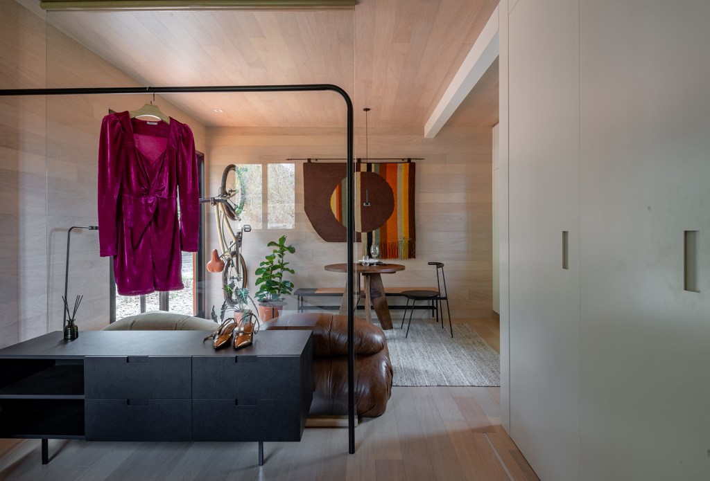 Tiny house sustentável de madeira fica pronta em 1 mês. Na foto, sala de estar com tapecaria na parede, mesa e plantas.