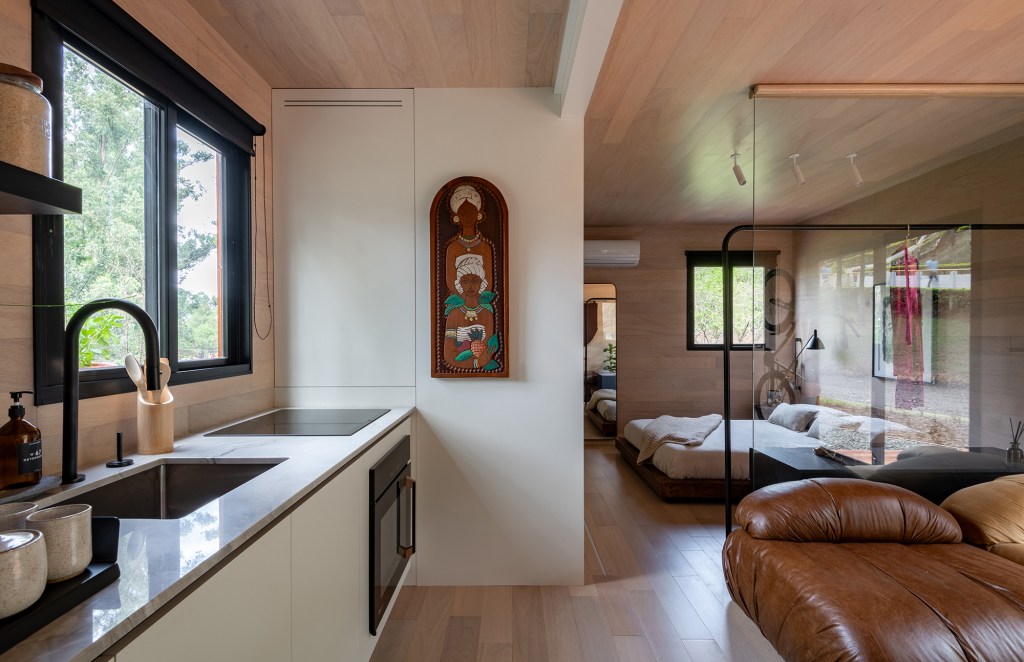 Tiny house sustentável de madeira fica pronta em 1 mês. Na foto, sala, quarto e cozinha integrados, Parede de madeira, sofá e cama.
