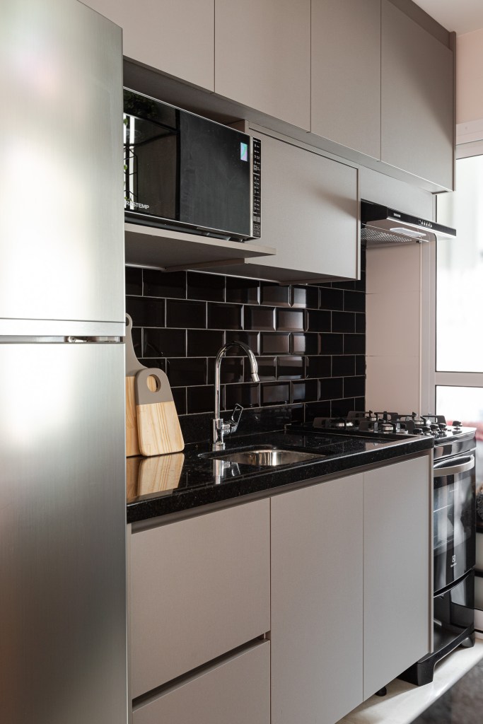 Projeto de Inovando Arquitetura. Na foto, cozinha com marcenaria cinza clara, bancada preta e backsplash de tijolinhos pretos.