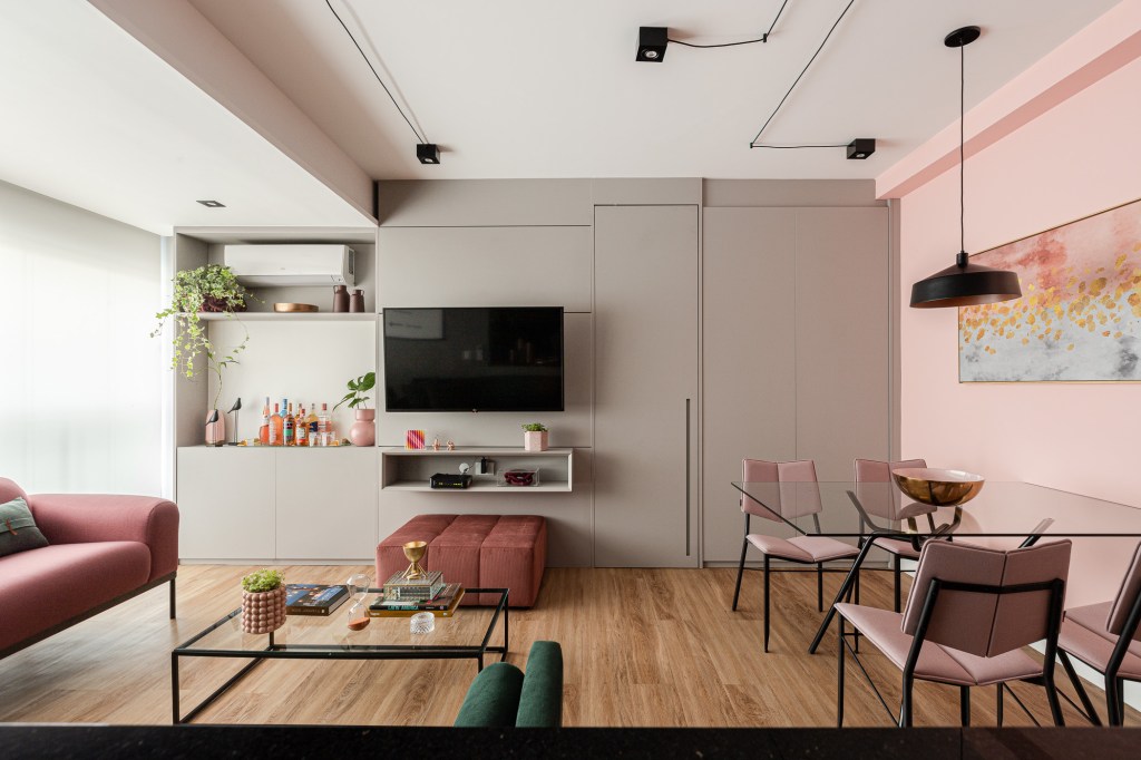 Projeto de Inovando Arquitetura. Na foto, sala de estar integrada com trilhos de iluminação aparentes, parede rosa e parede cinza.