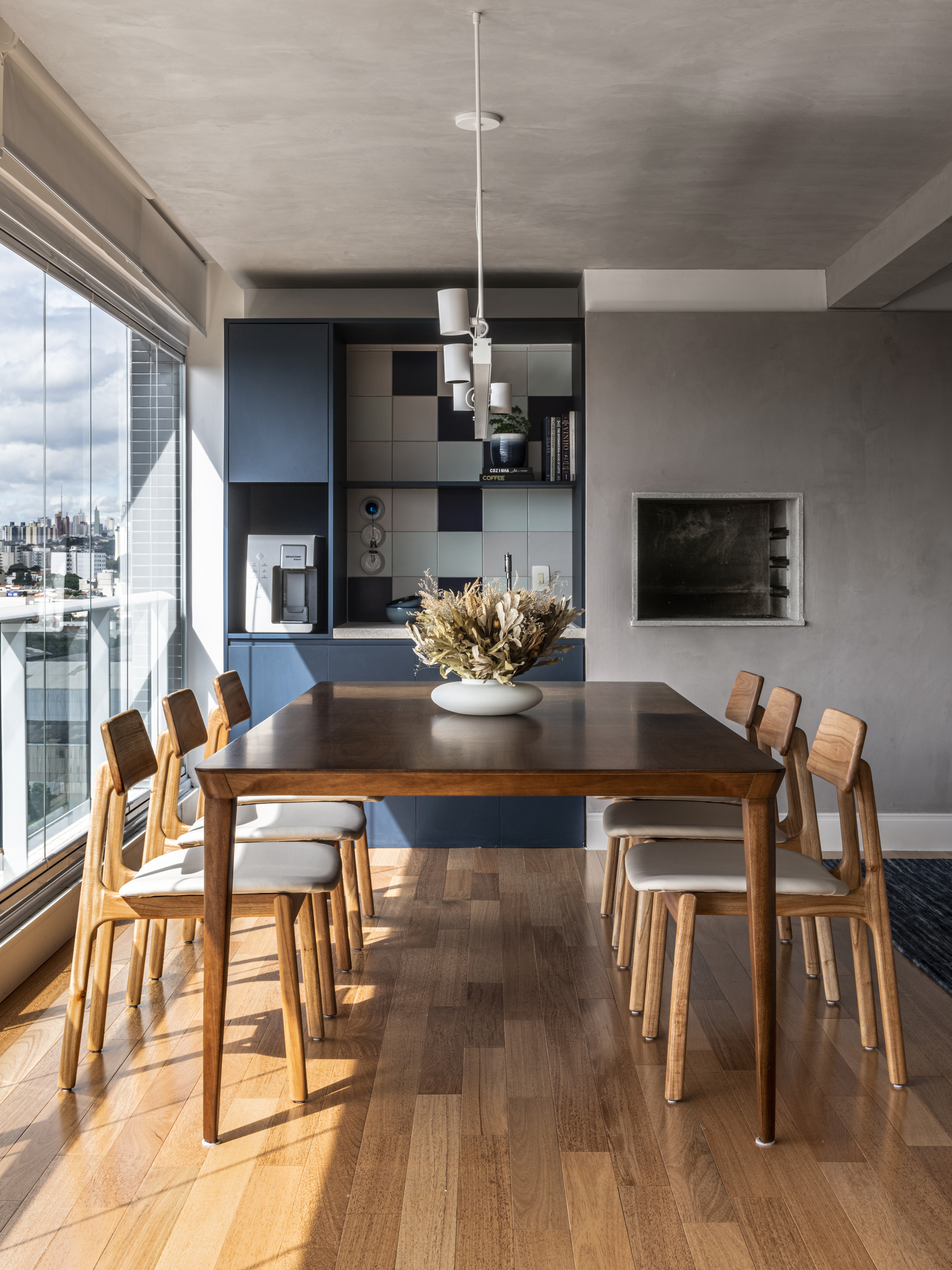 Apartamento de 130m² com projeto de M² Arquitetura. Na foto, varanda gourmet com mesa de madeira e churrasqueira.