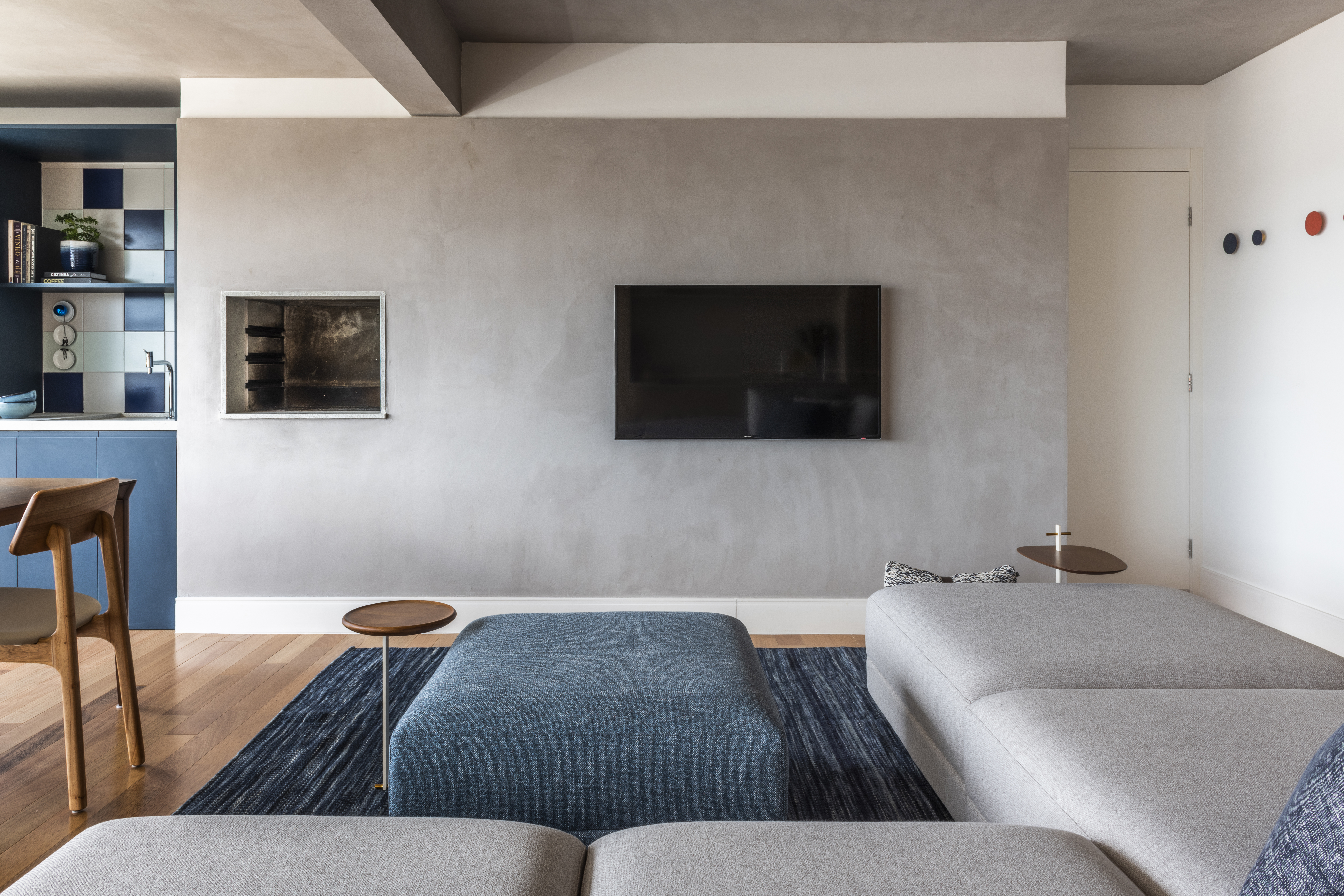 Apartamento de 130m² com projeto de M² Arquitetura. Na foto, sala de estar com sofá cinza, pufe azul e parede de cimento queimado.