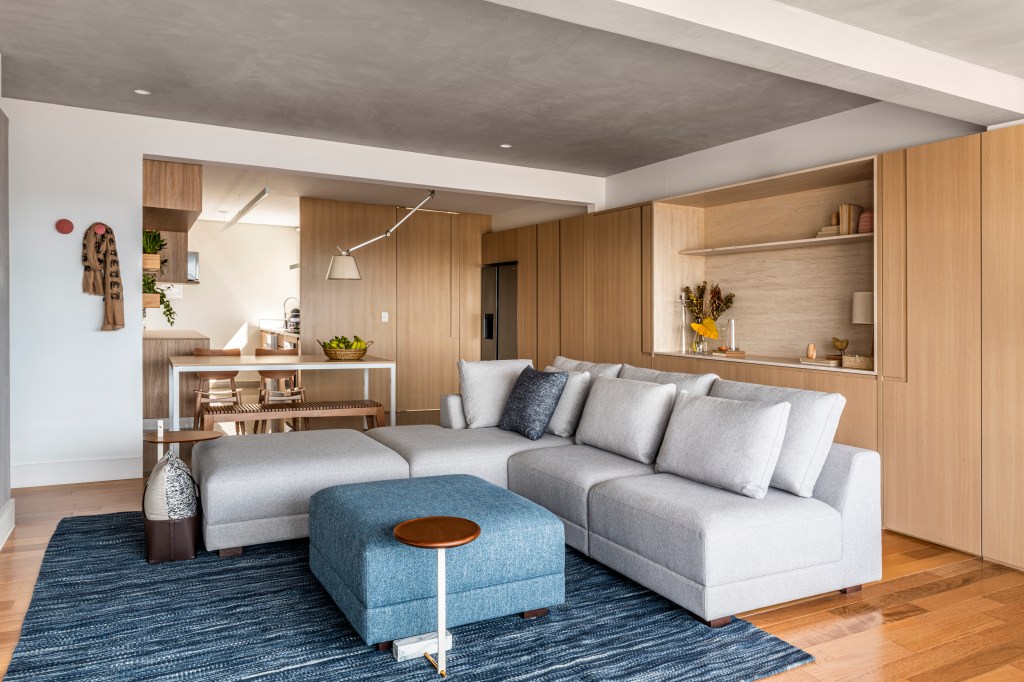 Apartamento de 130m² com projeto de M² Arquitetura. Na foto, sala integrada com sofá cinza claro, pufe azul e tapete azul.