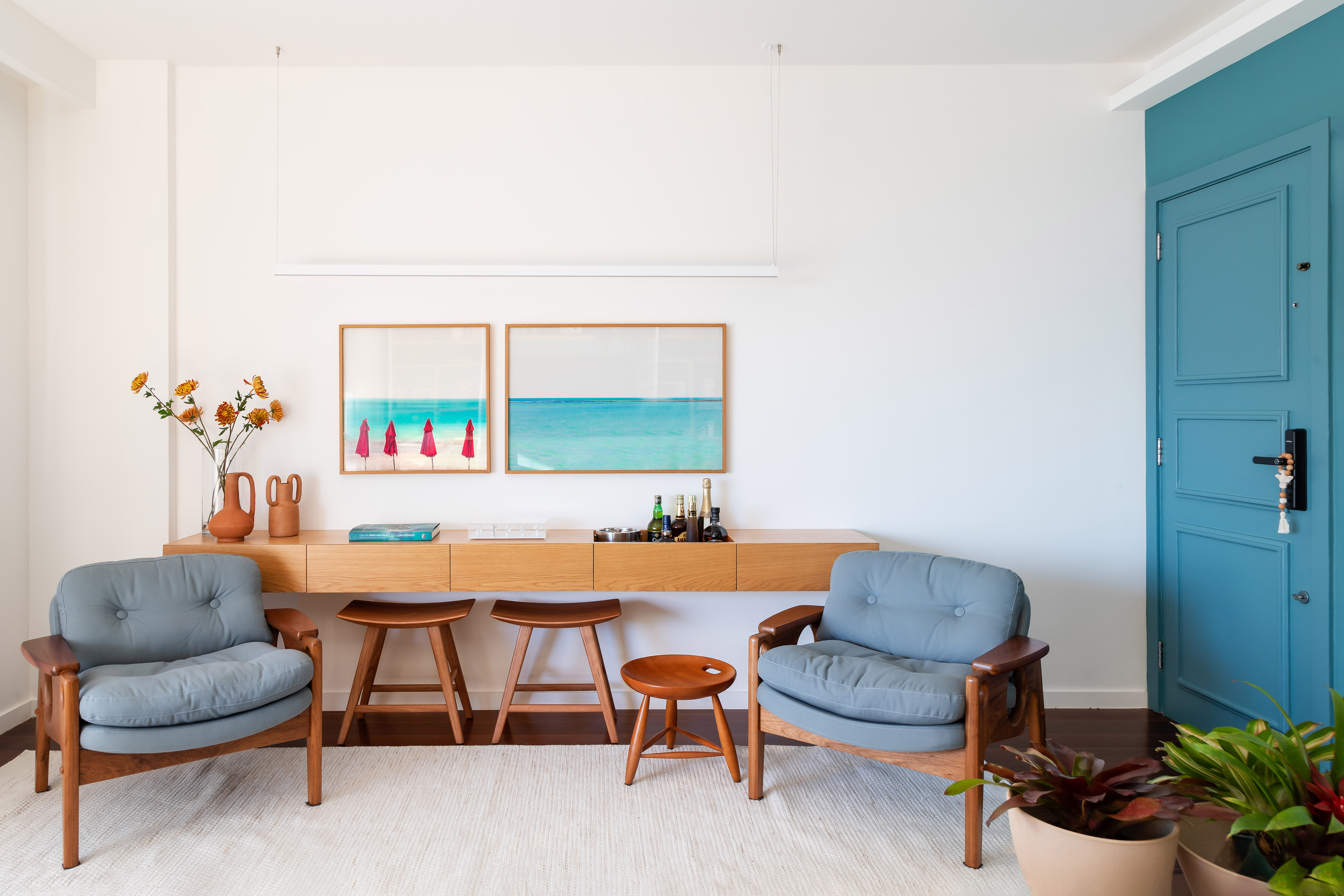 Projeto de MR Arquitetura. Na foto, sala de estar com parede branca, aparador de madeira, poltrona azul baixa.