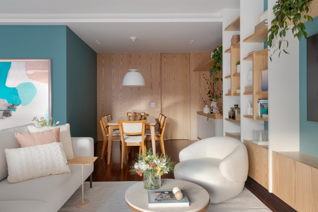 Projeto de MR Arquitetura. Na foto, sala de estar com parede azul, estante de nichos e poltronas brancas baixas; sala de jantar integrada.