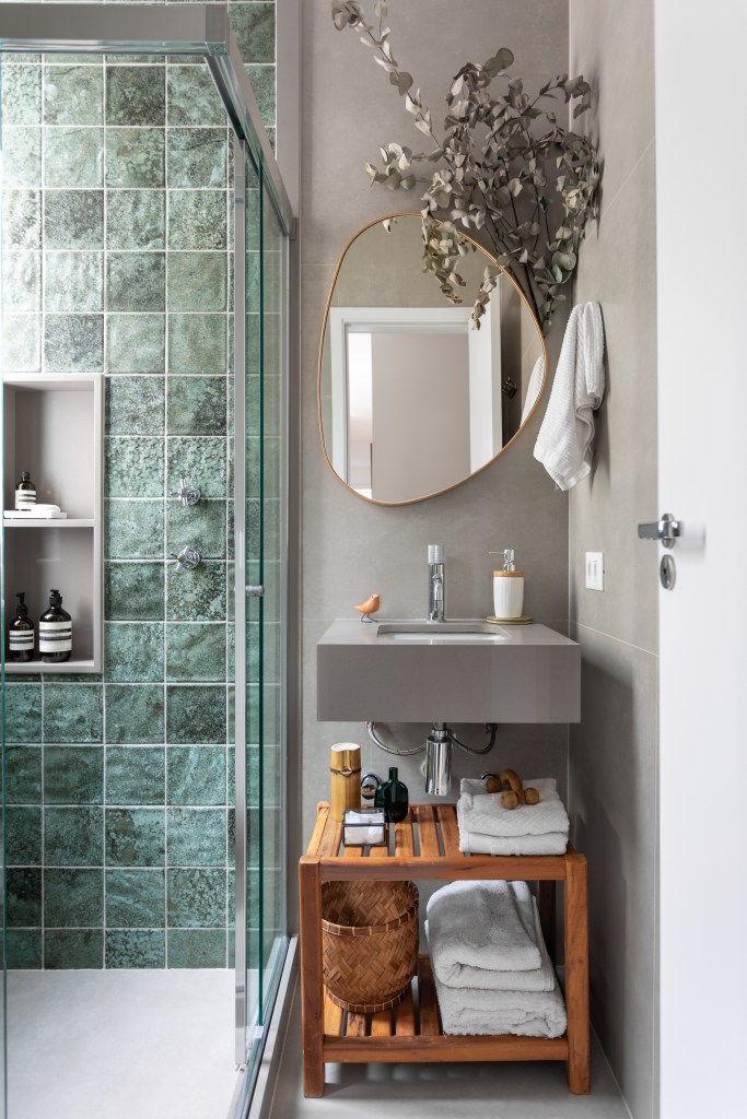 Projeto de Raphael Assaf Arquitetura. Na foto, banheiro pequeno com parede de azulejos azuis, espelho em forma orgânica.