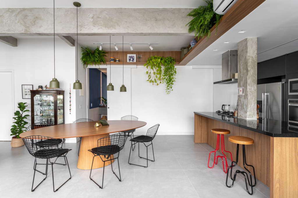 Projeto de Raphael Assaf Arquitetura. Na foto, cozinha integrada com sala de jantar. Mesa de madeira, prateleiras com plantas e piso de porcelanato.