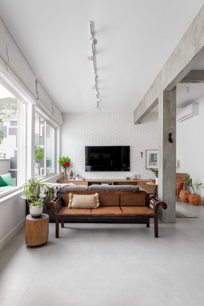 Projeto de Raphael Assaf Arquitetura. Na foto, sala de estar industrial com vigas de concreto, banco de madeira e tv.