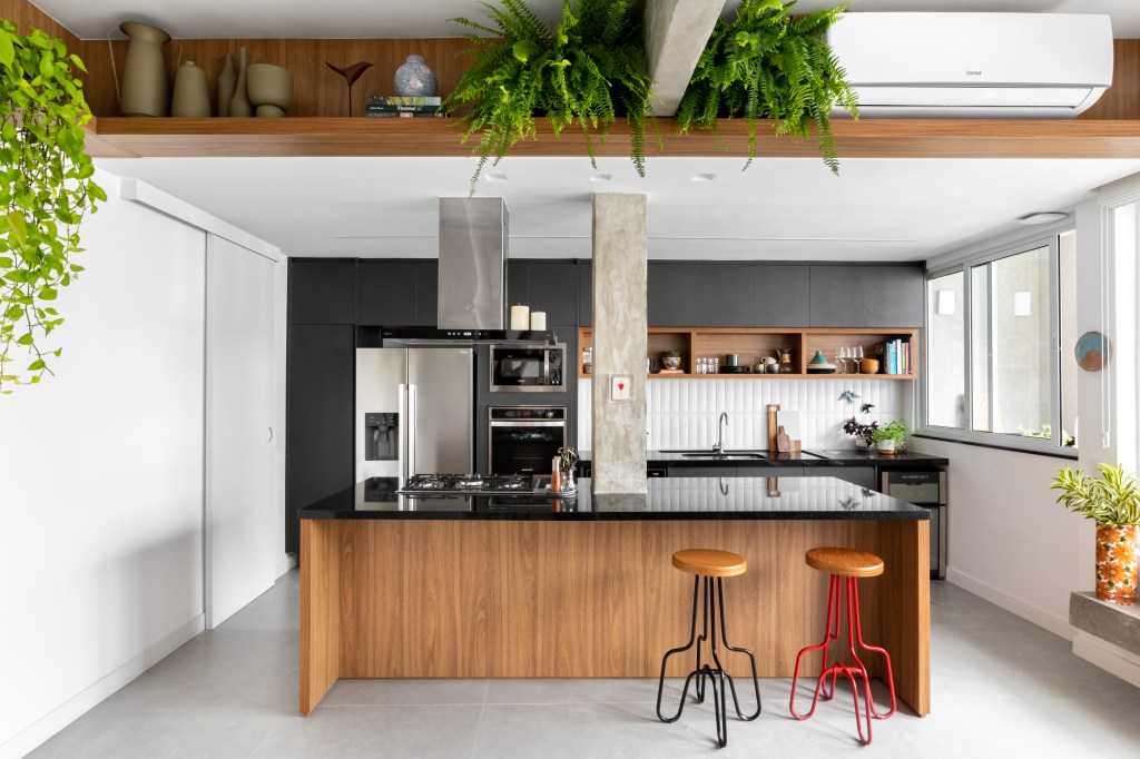 Projeto de Raphael Assaf Arquitetura. Na foto, cozinha americana integrada com ilha com bancada preta, banquetas e marcenaria preta.