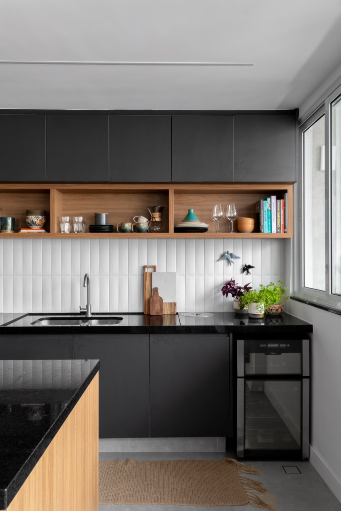 Projeto de Raphael Assaf Arquitetura. Na foto, cozinha americana integrada com marcenaria preta e backsplash de azulejos brancos.