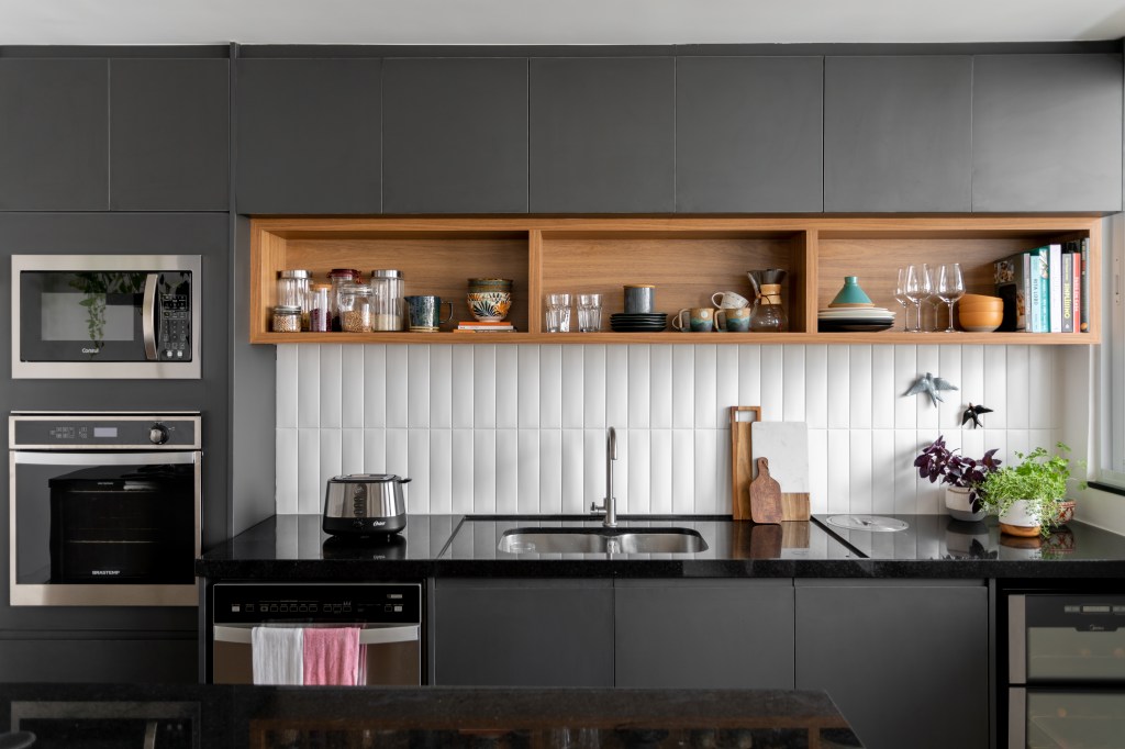 Projeto de Raphael Assaf Arquitetura. Na foto, cozinha americana integrada com marcenaria preta e backsplash de azulejos brancos.