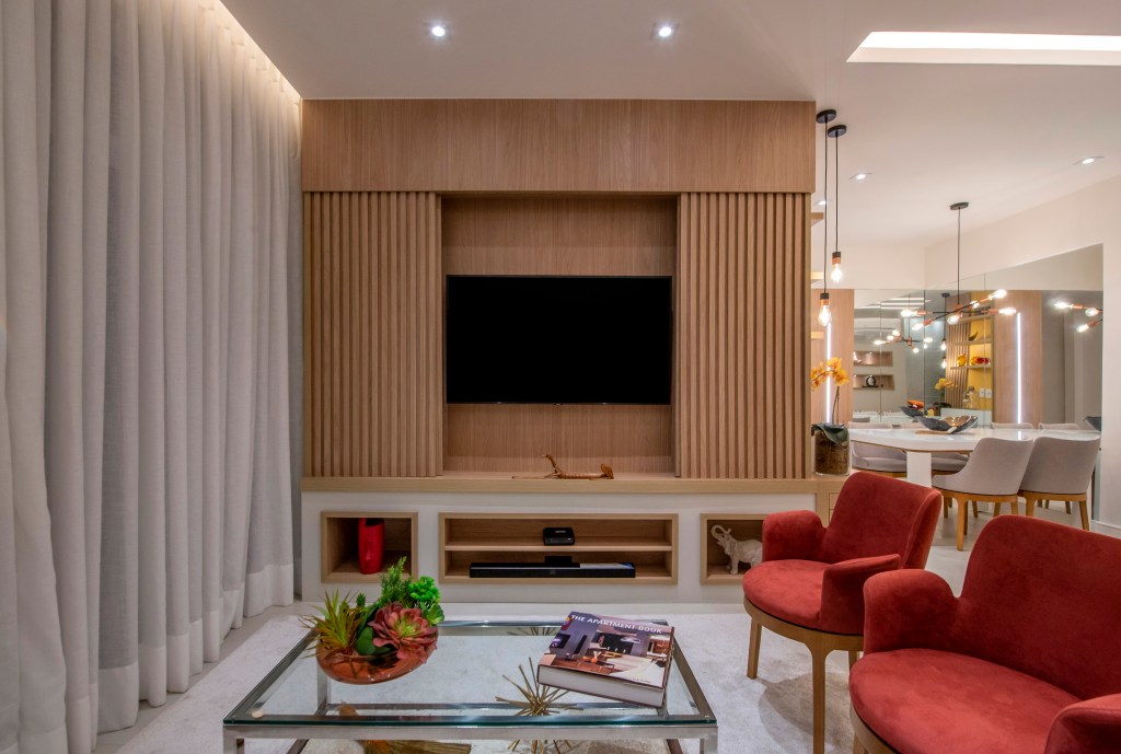 Apartamento de 85 m² tem décor baseada nas cores do chackras. Projeto de Campos & Olivetti Arquitetura. Na foto, sala de estar com painel de Tv e poltronas vermelhas.