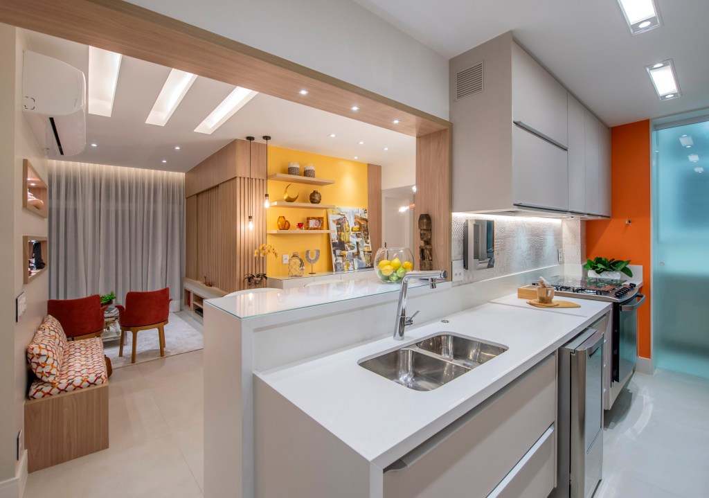 Apartamento de 85 m² tem décor baseada nas cores do chackras. Projeto de Campos & Olivetti Arquitetura. Na foto, sala estar com parede amarela e cozinha integrada,