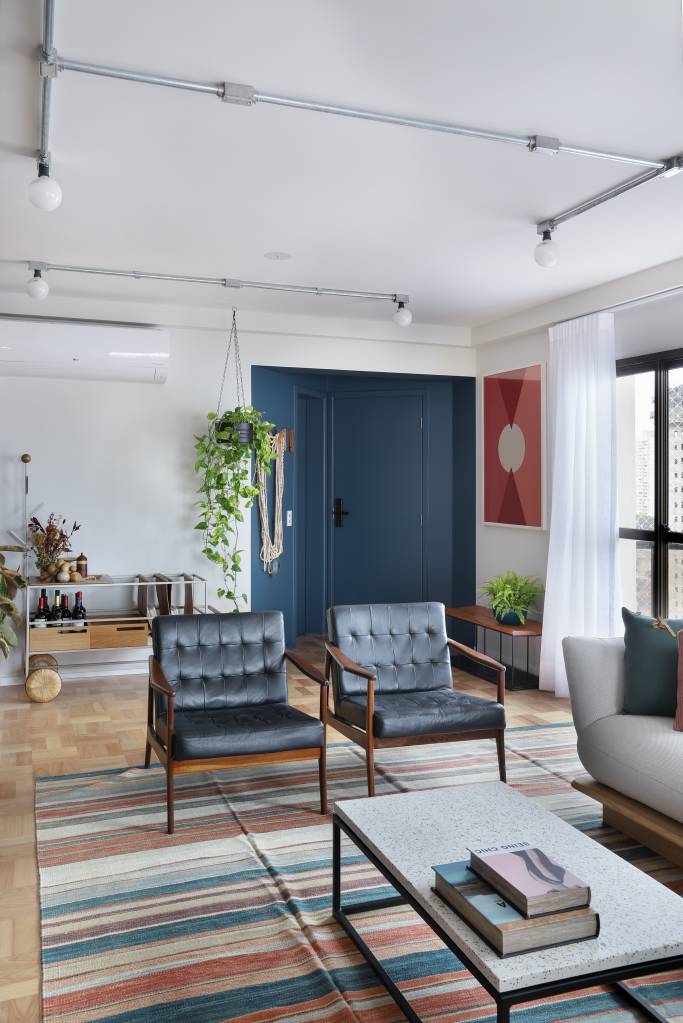 Apê de 180m² ganha color block azul na entrada e área de descompressão. Projeto de Studio 92 Arquitetura. Na foto, sala com poltronas azul escuro e tapete listrado colorido.