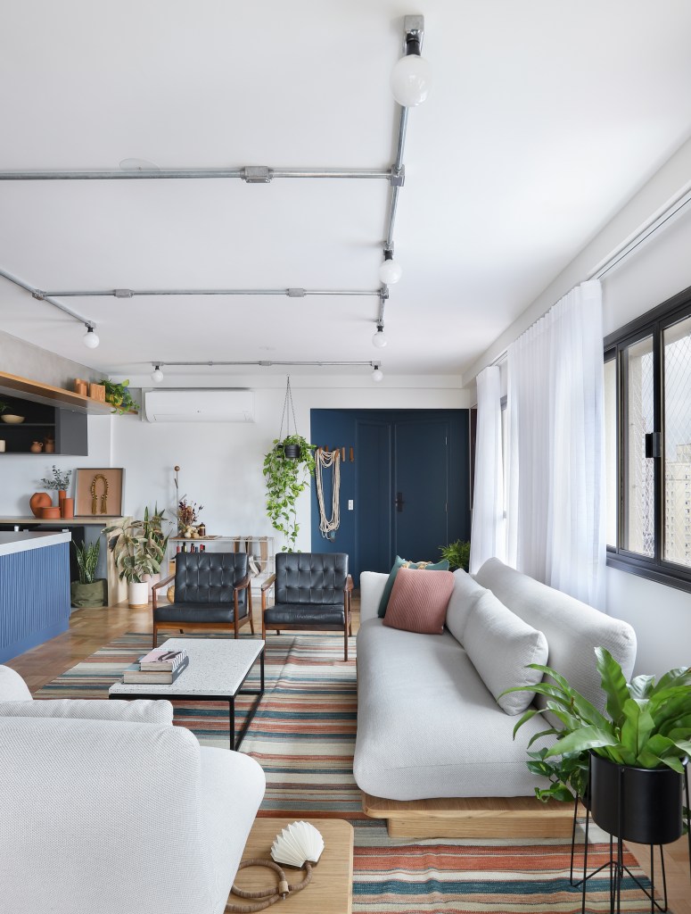 Apê de 180m² ganha color block azul na entrada e área de descompressão. Projeto de Studio 92 Arquitetura. Na foto, sala de estar integrada com cozinha com piso de taquinho e tapete colorido.