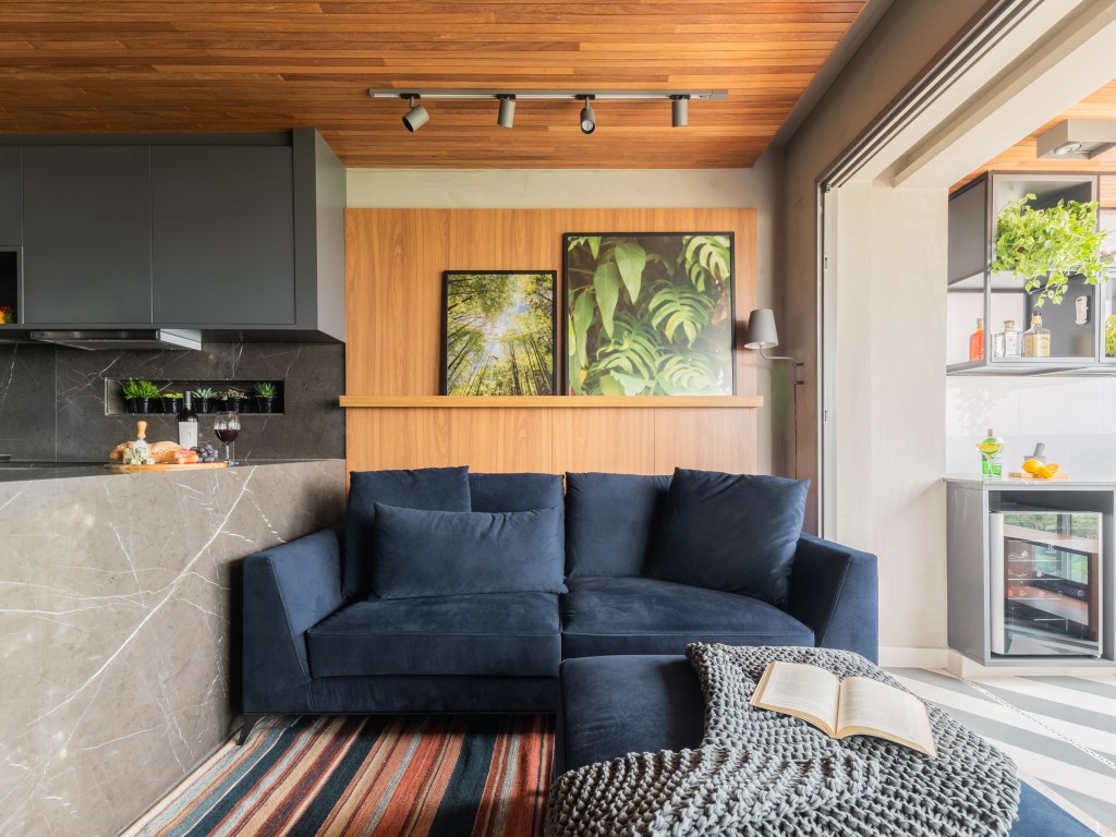 Apê de 64m² tem cozinha com bancada de mármore e forro de madeira. Projeto de Pietro Terlizzi. Na foto, sala com sofá azul marinho e tapete listrado.