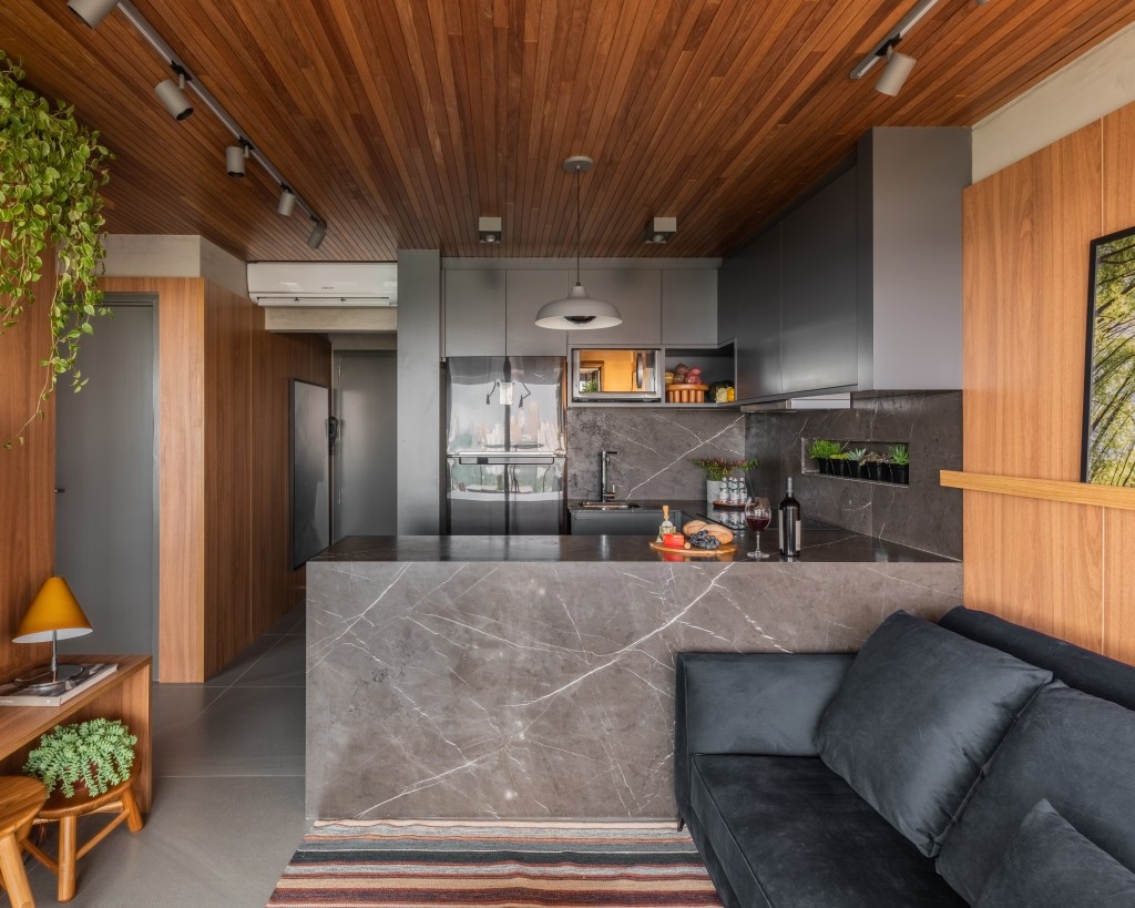 Apê de 64m² tem cozinha com bancada de mármore e forro de madeira. Projeto de Pietro Terlizzi. Na foto, cozinha com marcenaria cinza com armários com puxadores ocultos.