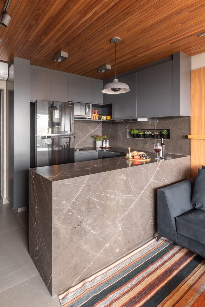 Apê de 64m² tem cozinha com bancada de mármore e forro de madeira. Projeto de Pietro Terlizzi. Na foto, cozinha com marcenaria cinza com armários com puxadores ocultos.