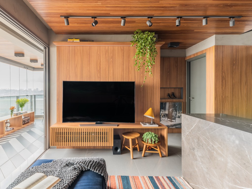 Apê de 64m² tem cozinha com bancada de mármore e forro de madeira. Projeto de Pietro Terlizzi. Na foto, sala de tv com parede revestida de madeira.