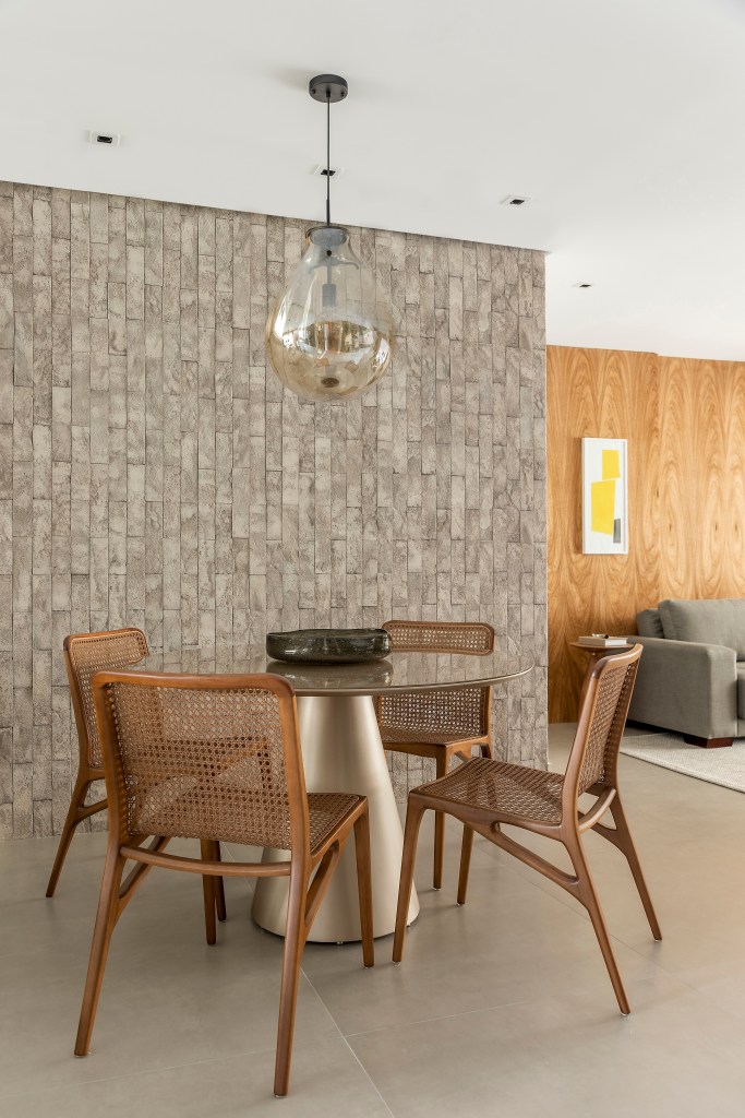 Projeto de Andrea Balastreire. Na foto, sala de jantar com mesa redonda, luminária e parede de tijolinhos cimentícios.