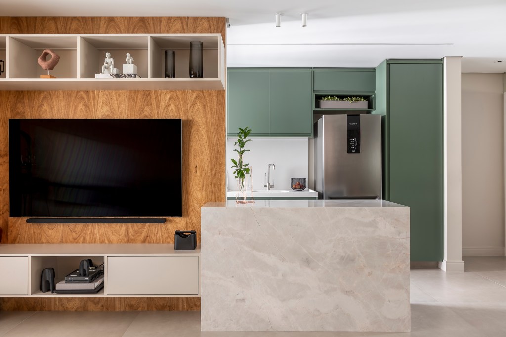 Projeto de Andrea Balastreire. Na foto, sala de tv integrada com cozinha. Armários verde musgo e bancada marmorizada.