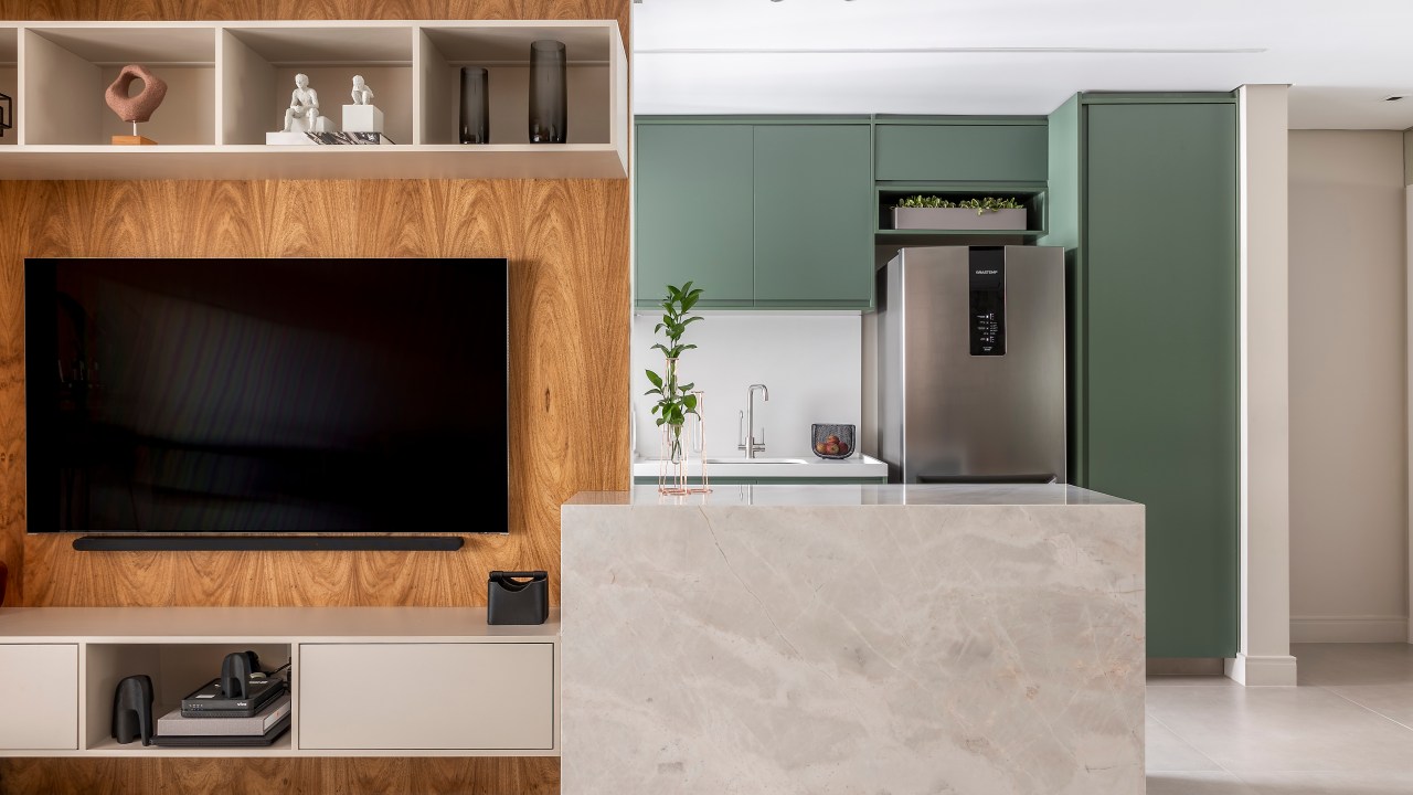 Projeto de Andrea Balastreire. Na foto, sala de tv integrada com cozinha. Armários verde musgo e bancada marmorizada.