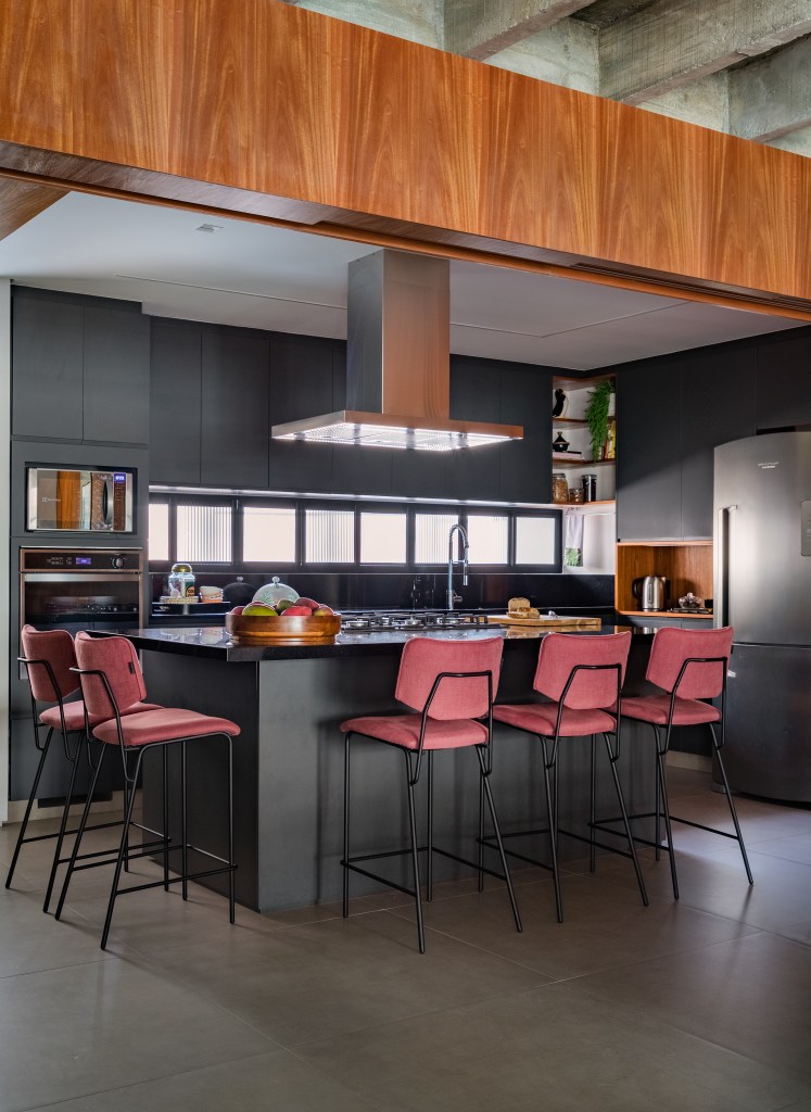 Projeto de Adriana Bersou. Na foto, cozinha integrada com marcenaria preta e banquetas rosa.
