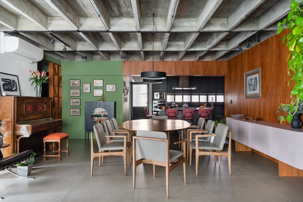 Projeto de Adriana Bersou. Na foto, sala de estar e jantar integradas com laje de concreto aparente e parede verde.