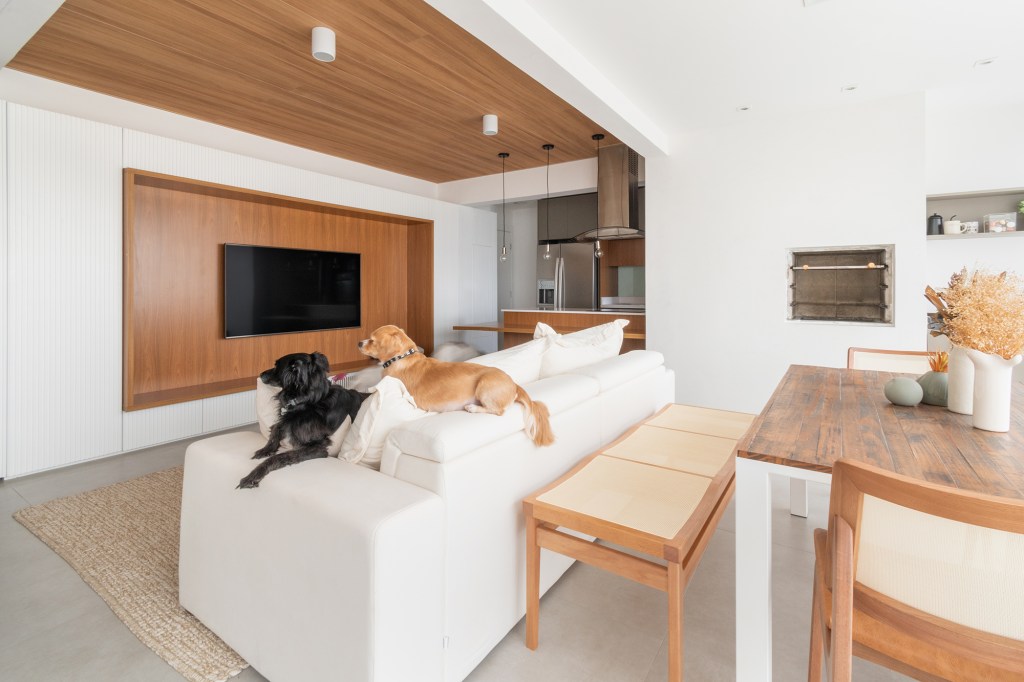 Apê minimalista de 100 m² foi pensado para os quatro cachorros da família. Projeto de Entre Studio. Na foto, varanda com espaço gourmet. poltrona de leitura e sala integrada.