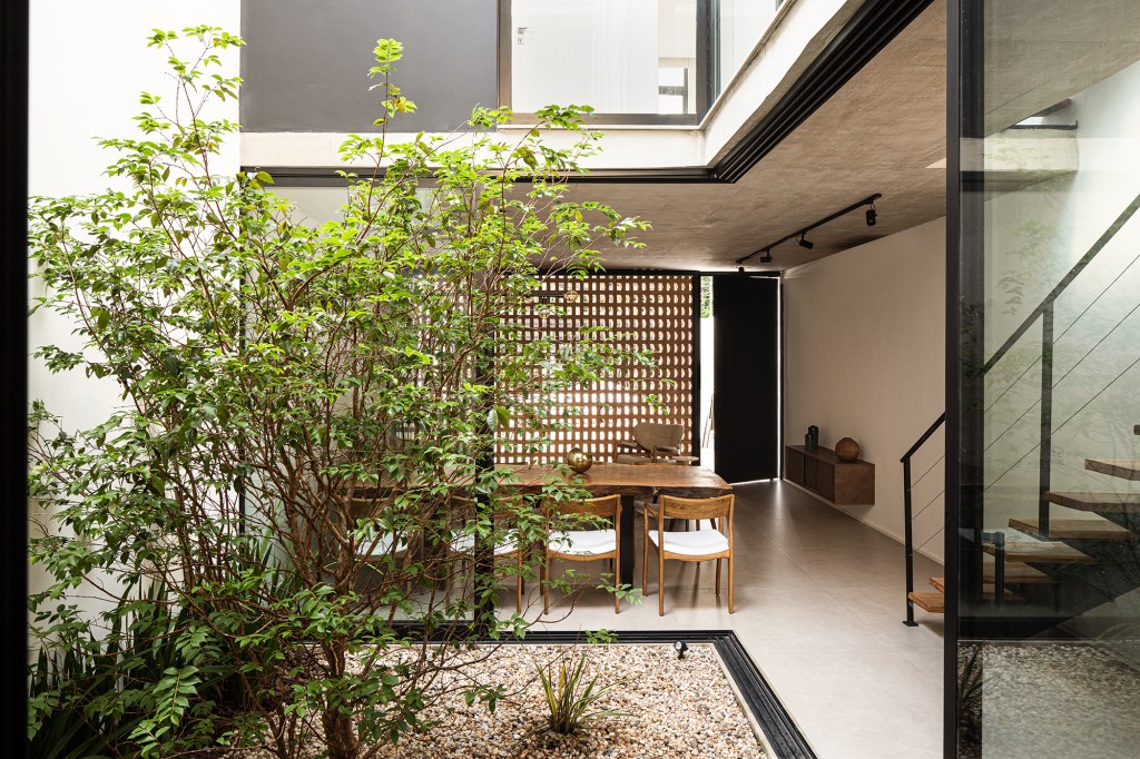Átrio central e fachada vazada de tijolos marcam projeto de casa de 220 m². Projeto Eixo Arquitetos. Na foto, sala de jantar com abertura para o jardim interno e escada.